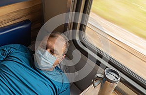 Man in a medical mask near the train car. concept of travel during the pandemic. passenger is lying in his seat in the compartment