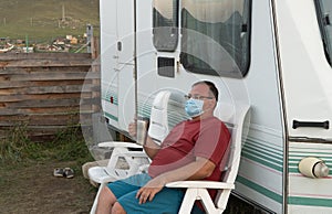 Man in a medical mask next to a tourist trailer. recreational vehicle RV. concept of travel during the pandemic. mode of permanent