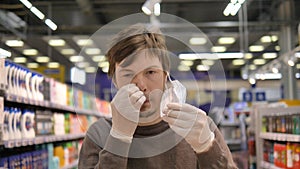 Man in a medical mask and rubber gloves in a supermarket removes the mask and scratches his nose and face. Neglects