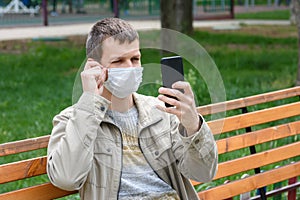 A man in a medical mask sits on a bench and adjusts the mask