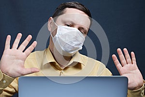 A man in a medical mask watches the news on a laptop. Makes a gesture of denial with palms. Protection against infection in self-