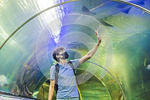Man in medical masks look at the fish in the aquarium in oceanarium. People walk in medical masks after the end of the