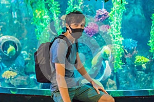 Man in medical masks look at the fish in the aquarium in oceanarium. People walk in medical masks after the end of the