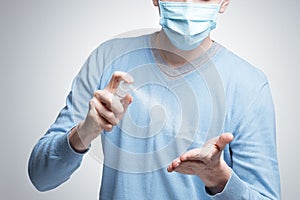 A man in a medical protective masked face mask, a means of protection against the virus, uses a spray to disinfect hands. Epidemia