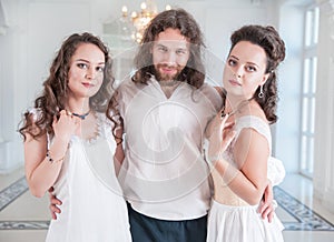 Man in medieval costume and two beautiful woman in old-fashioned negligee