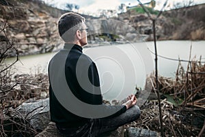 Man meditating on rocky cliff with river view