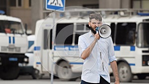 Man with megaphone shouts on street in the city against backdrop of a police car