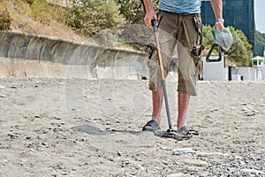 A man with a metal detector on a sandy beach in the daytime in summer.