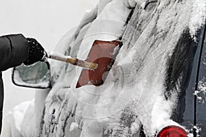 A man with a metal shovel cleans car from snow on the street after big snowstorm in the city, all cars under snow, icy roads, snow