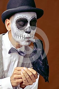 Man with mexican calaveras makeup kissing a black crow