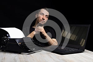 Man midway between a typewriter and laptop on black background in low key.The concept of the past and the future