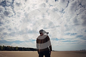 Man in a military gas mask stands on deserted shore against cloudy sky. Human silhouette in a gas mask, side view. Apocalypse