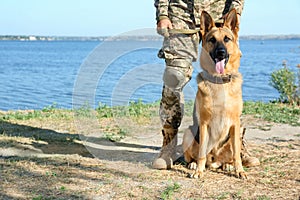 Man in military uniform with German shepherd dog near river, closeup