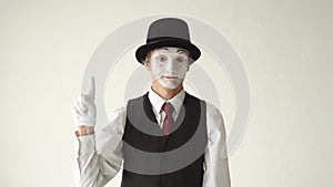 Man mime standing on white background and looking to the camera. Finger waves side to side to express `no` or `tsk tsk.`
