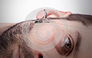 Man with miniature lawnmower shaving his own giant face