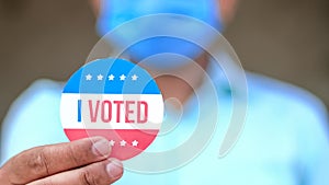 Man from minority group holds I Voted sticker upclose to the camera rackfocus