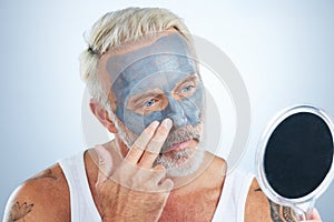 Man, mirror and clay mask for face skincare, wellness and organic cleaning with smile by studio background. Elderly male