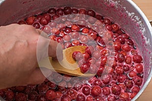 A man mixes a wooden spoon cherry jam.
