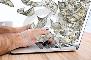 Man with modern laptop and flying dollar banknotes at table. People make money online