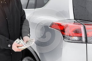 Man with money near car. Money dollars in car fuel tank.