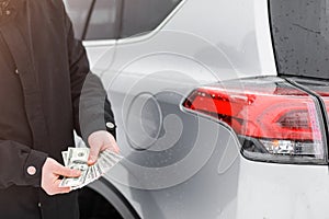 Man with money near car. Money dollars in car fuel tank.