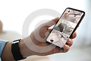 Man monitoring CCTV cameras on smartphone indoors, closeup. Home security system
