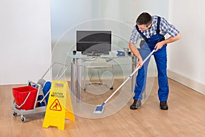 Man mopping office with wet floor sign