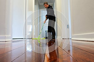 Man mopping a wooden floor at home corridor