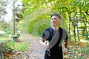 Man on morning jog in autumn park, asian sportsman in sportswear with headphones and phone in forest listens to music on