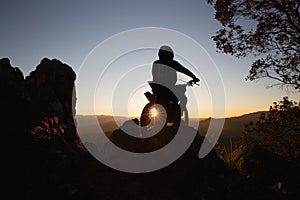 Man with motocross bike against beautiful lights, silhouette of a man with motocross motorcycle On top of rock high mountain at