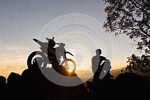 Man with motocross bike against beautiful lights, silhouette of a man with motocross motorcycle On top of rock high mountain at