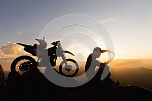 Man with motocross bike against beautiful lights, silhouette of a man with motocross motorcycle On top of rock high mountain at