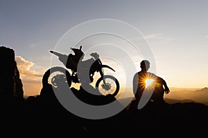 Man with motocross bike against beautiful lights, silhouette of a man with motocross motorcycle On top of rock high mountain at