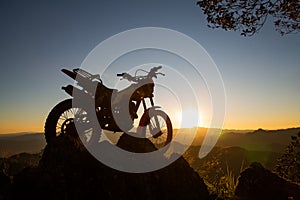 Man with motocross bike against beautiful lights, silhouette of a man with motocross motorcycle On top of rock high mountain at