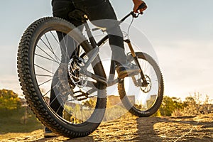 Man on mountain bike. Bicycle wheels close up image on sunset. Low angle view of cyclist riding mountain bike. Foot on
