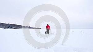 Man with mountain bike on snowy filed. Biker is pushing bike in deep snow. Cloudy winter day with gentle wind and snow flakes
