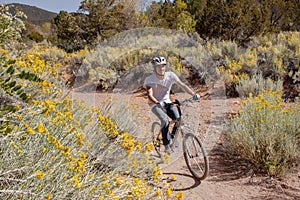 Man mountain biking on Atalaya Mountain Trail in Santa Fe, New Mexico surrounded by yellow brittlebush plants in the high desert