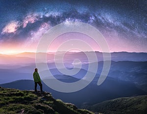 Man on the mountain peak and arched Milky Way over mountains