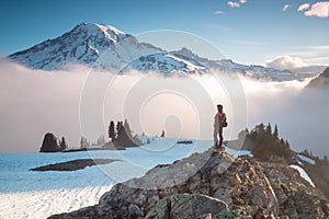 Man on the mountain peak looking on mountain valley with low clouds at colorful sunrise in autumn in Mount Rainier National park.