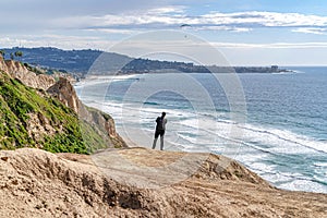 Man on mountain with view of the ocean with pier and parachuters in San Diego