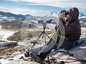 Man in the mountains looking through binoculars under blue sky
