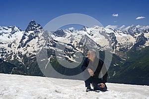 A man in the mountains took off his hat and knelt on a snowy peak, bowing to the beauty of the mountains