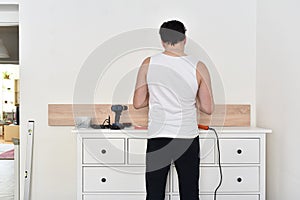 Man mounting shelves on the wall. All necessary tools are placed on the chest of drawers