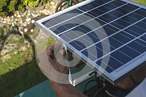 A man mounting a small 50 watt Polycrystalline solar panel on the eaves of a roof of a bungalow house