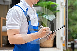 Man mover worker in blue uniform checking lists on clipboard while unloading cardboard boxes from truck