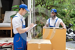 Man mover worker in blue uniform checking lists on clipboard while unloading cardboard boxes from truck