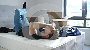 Man Moving Into New Home Using Mobile Phone Lying On Bed