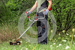 Man mowing the grass at his garden by using string trimmer