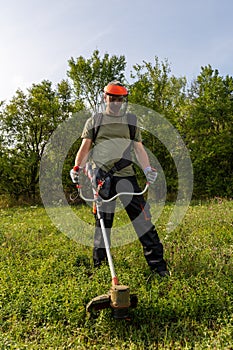 Man mowing the grass at his garden by using string trimmer with protective helmet and gloves