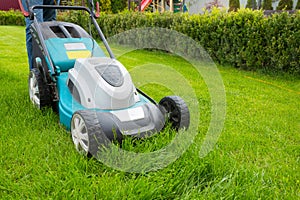 A man mowing grass with a lawn mower in the garden on a sunny day. A lawn mower on the lawn, a close-up